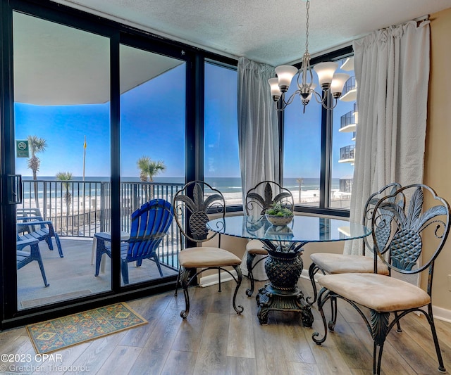 dining room featuring expansive windows, a textured ceiling, wood-type flooring, a notable chandelier, and a water view