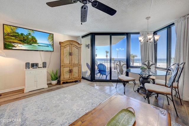 dining room featuring ceiling fan with notable chandelier, a textured ceiling, a wall of windows, a water view, and hardwood / wood-style flooring