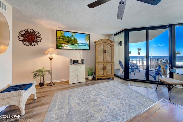 living room featuring ceiling fan, a textured ceiling, a wall of windows, and hardwood / wood-style floors