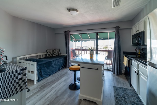 bedroom with a textured ceiling, access to outside, light wood finished floors, and visible vents