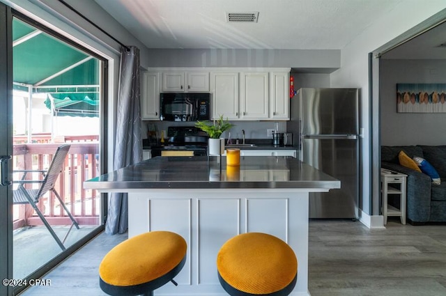 kitchen with black microwave, visible vents, white cabinetry, freestanding refrigerator, and range