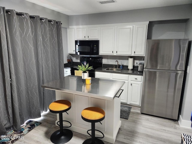 kitchen featuring white cabinets, dark countertops, a breakfast bar area, black appliances, and a sink