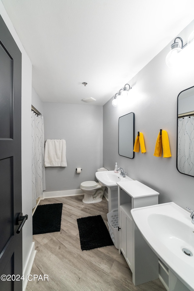 full bath featuring two sinks, wood finished floors, toilet, and baseboards