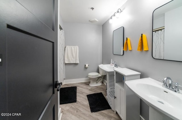 bathroom featuring toilet, two sinks, baseboards, and wood finished floors