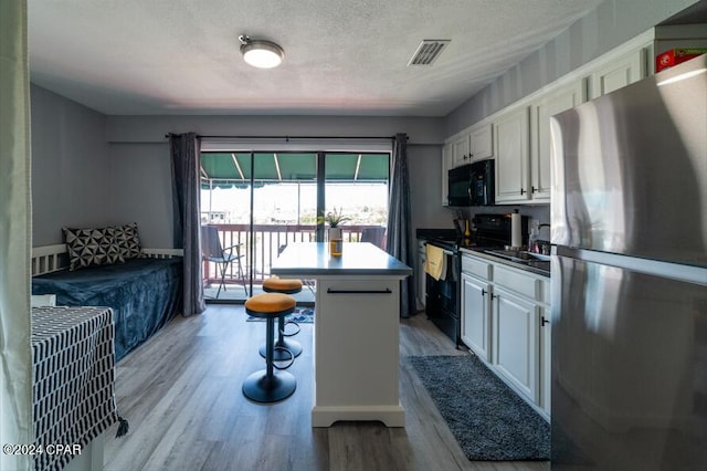 kitchen featuring black appliances, light wood finished floors, visible vents, and white cabinets