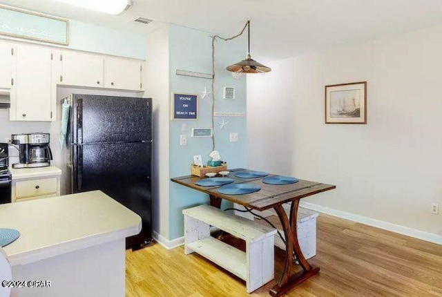 kitchen with black refrigerator, white cabinetry, hanging light fixtures, and light hardwood / wood-style flooring