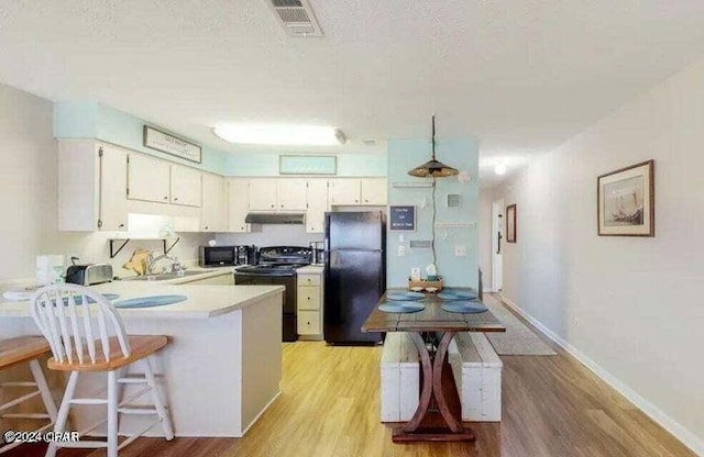 kitchen featuring kitchen peninsula, black refrigerator, light hardwood / wood-style floors, electric range oven, and a textured ceiling