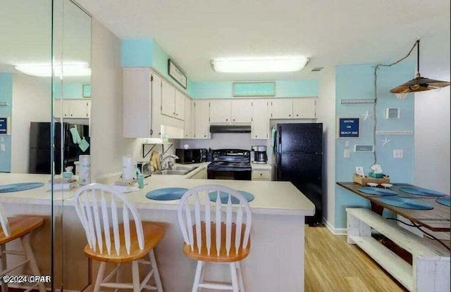 kitchen featuring kitchen peninsula, electric range, black refrigerator, a breakfast bar, and light hardwood / wood-style flooring