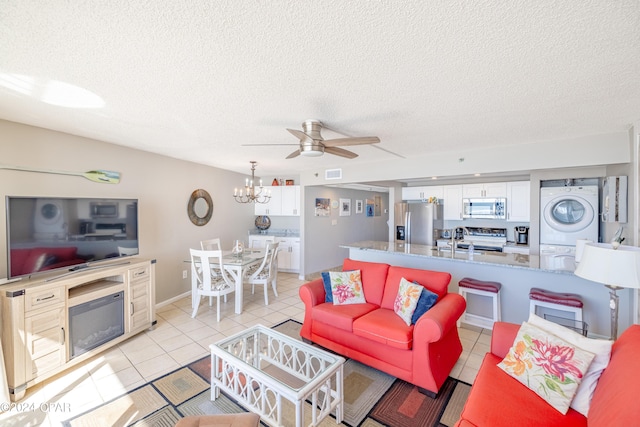 tiled living room with a textured ceiling, sink, stacked washer and dryer, and ceiling fan with notable chandelier