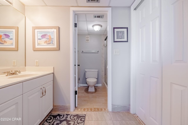 bathroom with a drop ceiling, vanity, toilet, and walk in shower