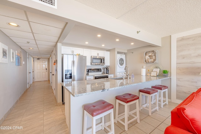 kitchen featuring sink, stainless steel appliances, stacked washing maching and dryer, white cabinets, and light stone countertops