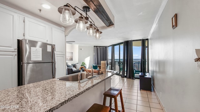 kitchen with sink, light stone counters, expansive windows, stainless steel refrigerator, and white cabinetry