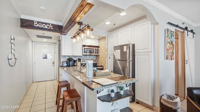 kitchen with a barn door, backsplash, white cabinets, and stainless steel appliances