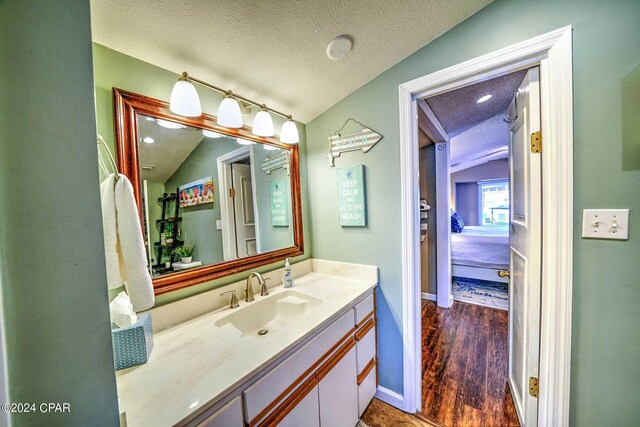 bathroom with a textured ceiling, wood-type flooring, vaulted ceiling, and vanity