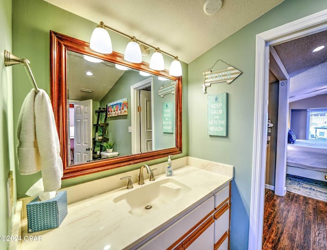 bathroom featuring vaulted ceiling, vanity, hardwood / wood-style floors, and a textured ceiling