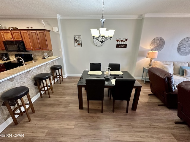 dining area with ornamental molding, an inviting chandelier, light hardwood / wood-style floors, and a textured ceiling