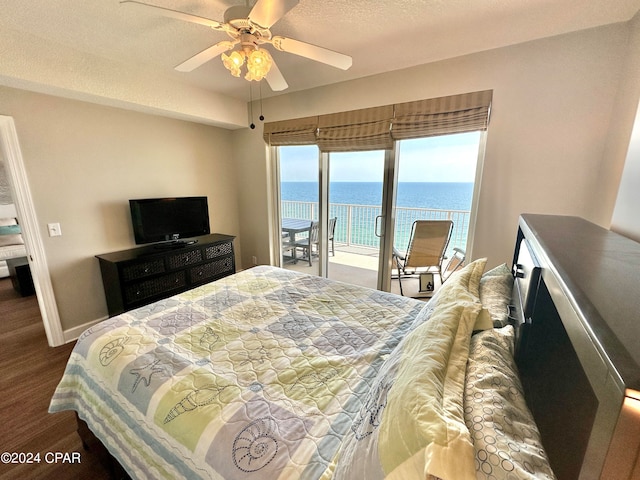 bedroom with dark hardwood / wood-style floors, access to exterior, a water view, ceiling fan, and a textured ceiling