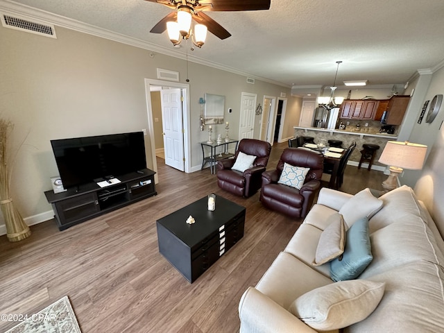 living room featuring ceiling fan with notable chandelier, crown molding, a textured ceiling, and hardwood / wood-style floors