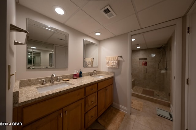 bathroom with a tile shower, dual sinks, tile flooring, vanity with extensive cabinet space, and a drop ceiling