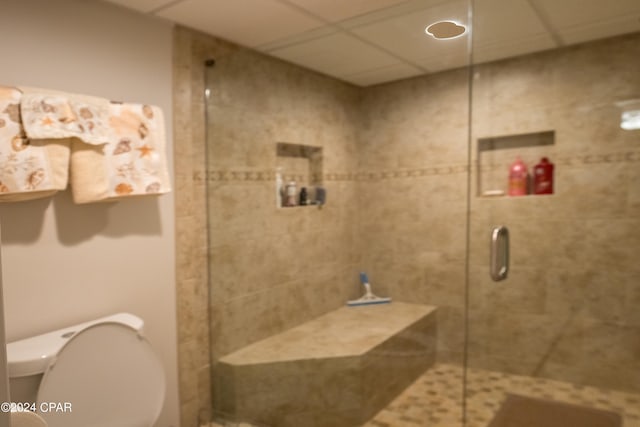 bathroom with toilet, an enclosed shower, and a drop ceiling