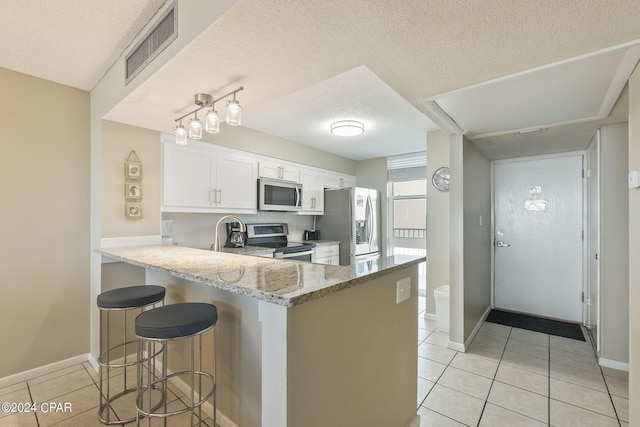 kitchen with white cabinetry, light tile flooring, appliances with stainless steel finishes, a textured ceiling, and light stone counters