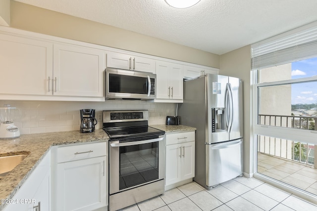 kitchen with light stone countertops, backsplash, appliances with stainless steel finishes, light tile floors, and white cabinets