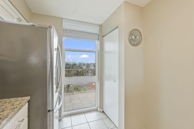 kitchen featuring stainless steel fridge, light tile flooring, white cabinetry, and light stone counters