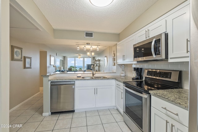 kitchen featuring light tile floors, appliances with stainless steel finishes, white cabinets, backsplash, and track lighting