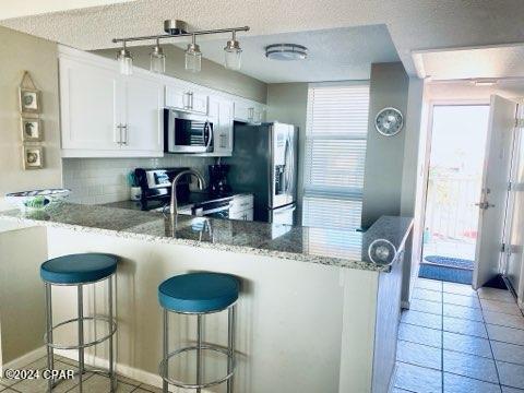 kitchen with white cabinets, appliances with stainless steel finishes, light stone counters, and kitchen peninsula