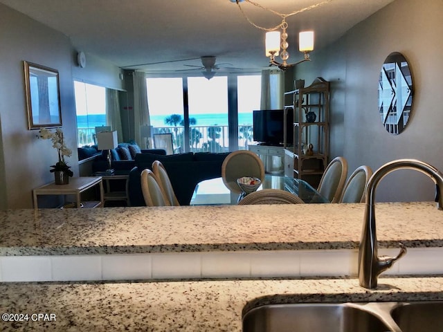 kitchen with pendant lighting, light stone countertops, ceiling fan with notable chandelier, a water view, and sink