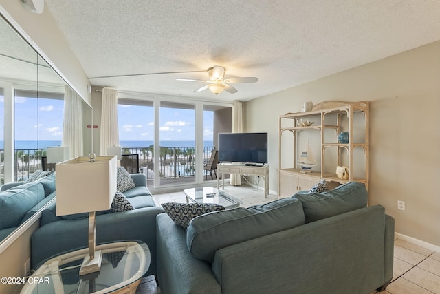 living room featuring ceiling fan, light tile floors, floor to ceiling windows, a water view, and a textured ceiling