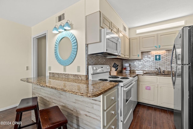 kitchen featuring a breakfast bar area, kitchen peninsula, white appliances, and dark stone countertops