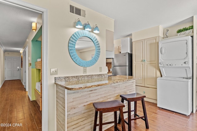 kitchen with stainless steel refrigerator, stacked washer / drying machine, light stone countertops, and light wood-type flooring