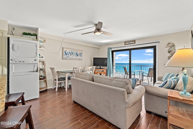 living room with a water view, dark hardwood / wood-style flooring, stacked washing maching and dryer, and ceiling fan