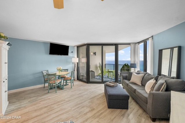 living room featuring ceiling fan, a wall of windows, a water view, and light wood-type flooring