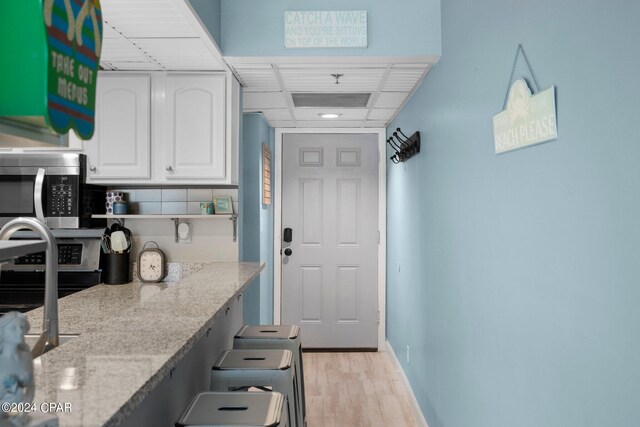 kitchen with white cabinets, range, light wood-type flooring, and light stone counters