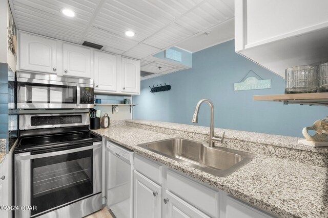 kitchen with stainless steel appliances, white cabinetry, light stone countertops, and sink