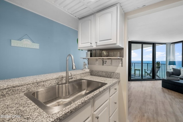 kitchen featuring light stone countertops, white cabinetry, sink, a water view, and hardwood / wood-style flooring