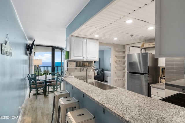 kitchen with stainless steel fridge, sink, light stone counters, a breakfast bar, and white cabinetry