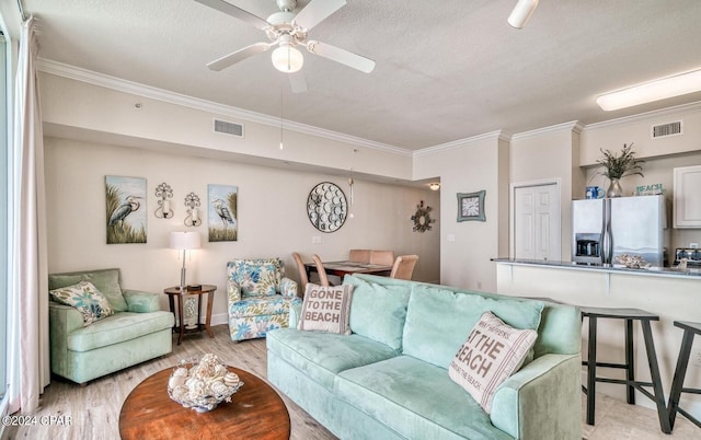 living room featuring light wood-type flooring, a textured ceiling, ceiling fan, and ornamental molding