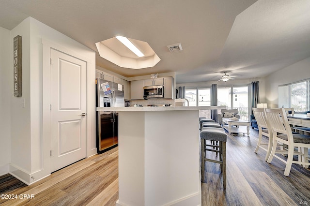 kitchen featuring a center island, light wood-type flooring, appliances with stainless steel finishes, a kitchen bar, and ceiling fan