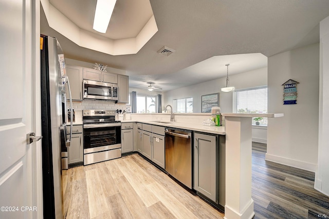 kitchen with kitchen peninsula, light hardwood / wood-style floors, stainless steel appliances, and gray cabinetry