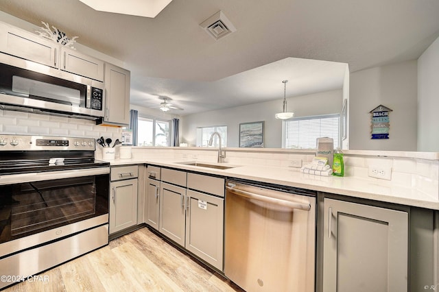 kitchen with kitchen peninsula, stainless steel appliances, sink, light hardwood / wood-style floors, and ceiling fan