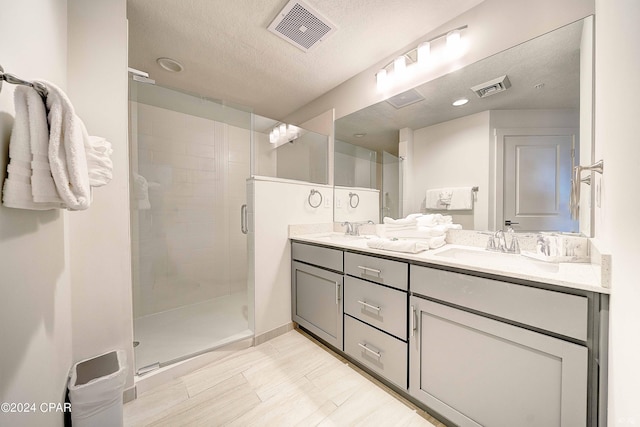 bathroom with dual sinks, a shower with shower door, a textured ceiling, and large vanity