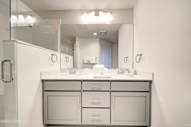 bathroom featuring a shower with shower door, a textured ceiling, and dual vanity