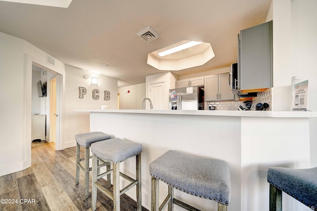 kitchen featuring gray cabinetry, hardwood / wood-style floors, backsplash, kitchen peninsula, and stainless steel fridge