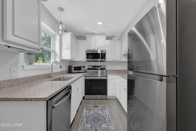 kitchen with hanging light fixtures, appliances with stainless steel finishes, sink, light hardwood / wood-style flooring, and white cabinets