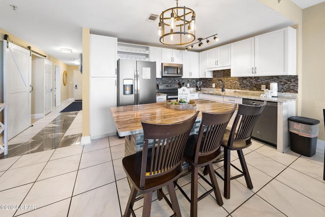 kitchen with a barn door, backsplash, appliances with stainless steel finishes, and white cabinets