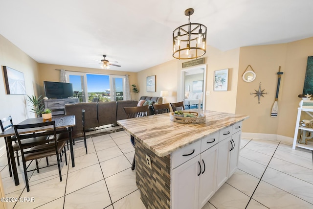 kitchen with a center island, baseboards, decorative light fixtures, ceiling fan with notable chandelier, and white cabinetry