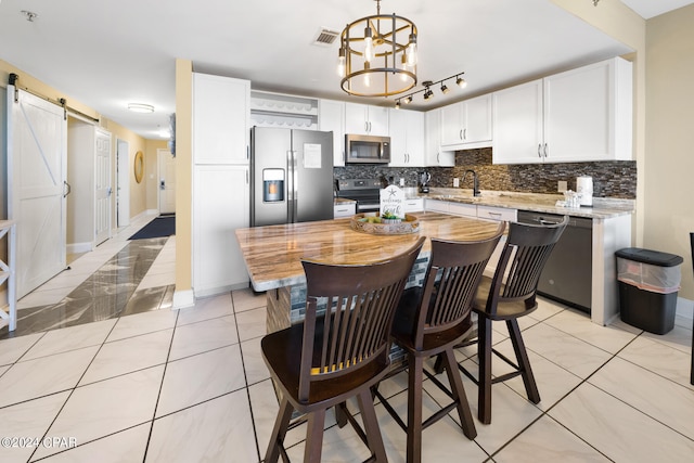 kitchen with white cabinets, backsplash, stainless steel appliances, a barn door, and a center island